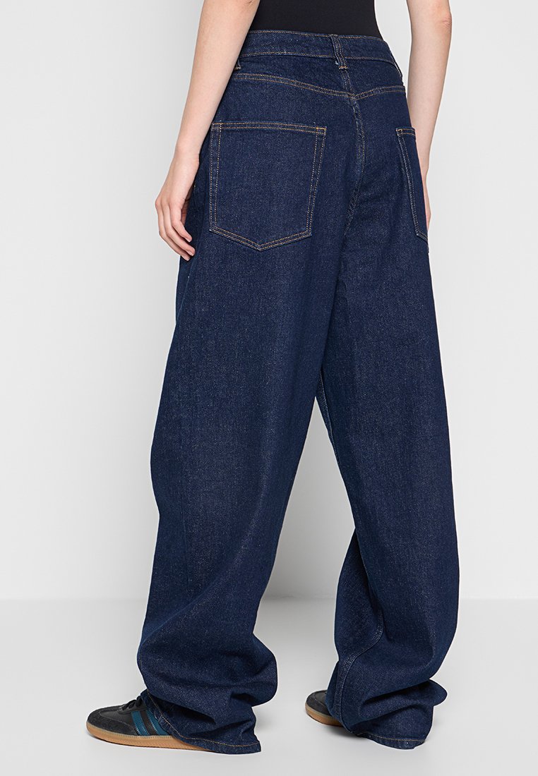 Pantaloni in denim blu scuro a gamba larga con vita alta, dotati di due tasche posteriori e dettagli di cucitura arancione a contrasto.