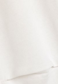 Tela de algodón blanca, de peso medio, textura suave con un ligero brillo. La costura en la parte inferior crea un aspecto de capa doblada.