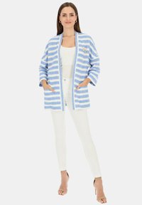 Jasnoniebieska i biała marynarka w paski z rękawami do łokci, otwarta z przodu, z bocznymi kieszeniami, zestawiona z białymi spodniami i szpilkami.