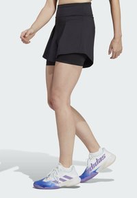 Sort sportskort over sorte shorts med høj talje. Skoene er primært hvide med lilla og blå accenter. Glat stofstruktur.