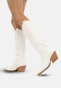 Botas blancas hasta la rodilla con bordado texturizado, puntera afilada y tacón apilado. Cuentan con una cremallera lateral para facilitar el uso. Acabado suave.