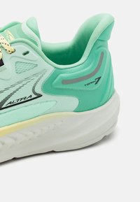 Scarpa da corsa di un verde menta chiaro con una tomaia in rete testurizzata, tallone imbottito e accenti riflettenti. Presenta una suola intermedia bianca e dettagli gialli.
