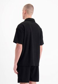 Zwart shirt met korte mouwen van textuurstof met een kraag, gecombineerd met bijpassende shorts. De stof heeft een subtiel patroon.