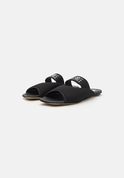 Sorte svarte sandaler med åpen tå og polstrede svarte stoffstropper. Har en glatt svart såle og hvit logodetalj på stroppen.