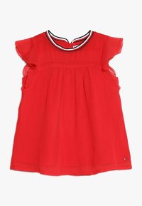 Haut rouge à manches courtes en tissu léger, présentant un décolleté rond avec une bordure contrastante noire et blanche et un design plissé.