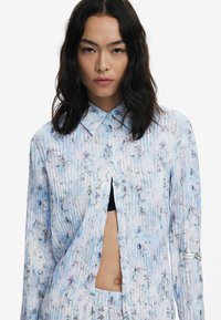 Long-sleeve shirt in lightweight fabric, featuring a blue and white floral pattern with vertical stripes, button closure, and cut-out detail.