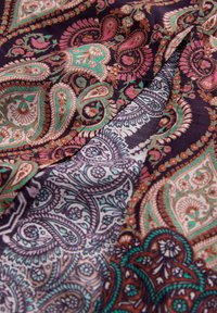 Tissu à motif paisley multicolore dans des tons profonds de violets, verts et roses, avec des détails complexes et une texture lisse.