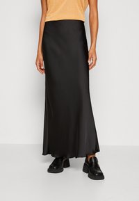 Zwarte satijnen maxirok met een fijne textuur, voorzien van een aansluitende tailleband en een vloeiende zoom. Gecombineerd met chunky zwarte schoenen.