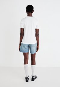 Vit bomull T-shirt med kort ärm, matchad med ljusblå denimshorts. Vita knähöga strumpor och svarta skor fulländar outfiten.