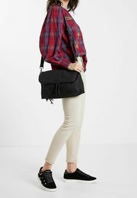 Sac bandoulière noir en nylon avec un rabat et un motif de papillon en relief ; sangle ajustable et fermeture éclair ; texture lisse.