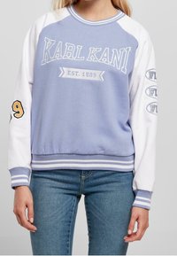 Světlé fialové mikina s bílými raglánovými rukávy. Obsahuje logo "KARL KANI EST. 1989" a detaily, žebrované manžety a lem.