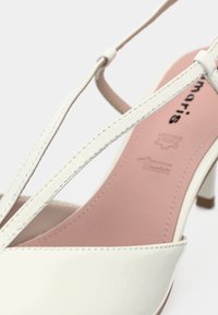 Sandale à talons hauts en cuir blanc avec des lanières étroites et une semelle intérieure rose embossée des marques de la marque et de qualité du cuir.