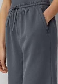 Grijze joggingbroek gemaakt van zacht textiel, met een elastische tailleband, verstelbaar trekkoord en zijzakken. Soepele textuur met subtiele stiksels.