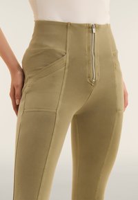 Leggings a vita alta in tessuto verde oliva, dotate di chiusura frontale con zip, tasche laterali e dettagli delle cuciture per un aspetto aderente.