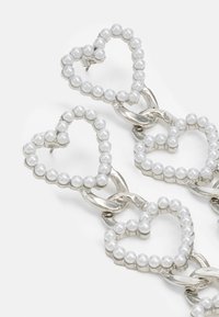 Silver chain earrings featuring heart-shaped designs adorned with white pearls along the edges, highlighting a lustrous, textured finish.