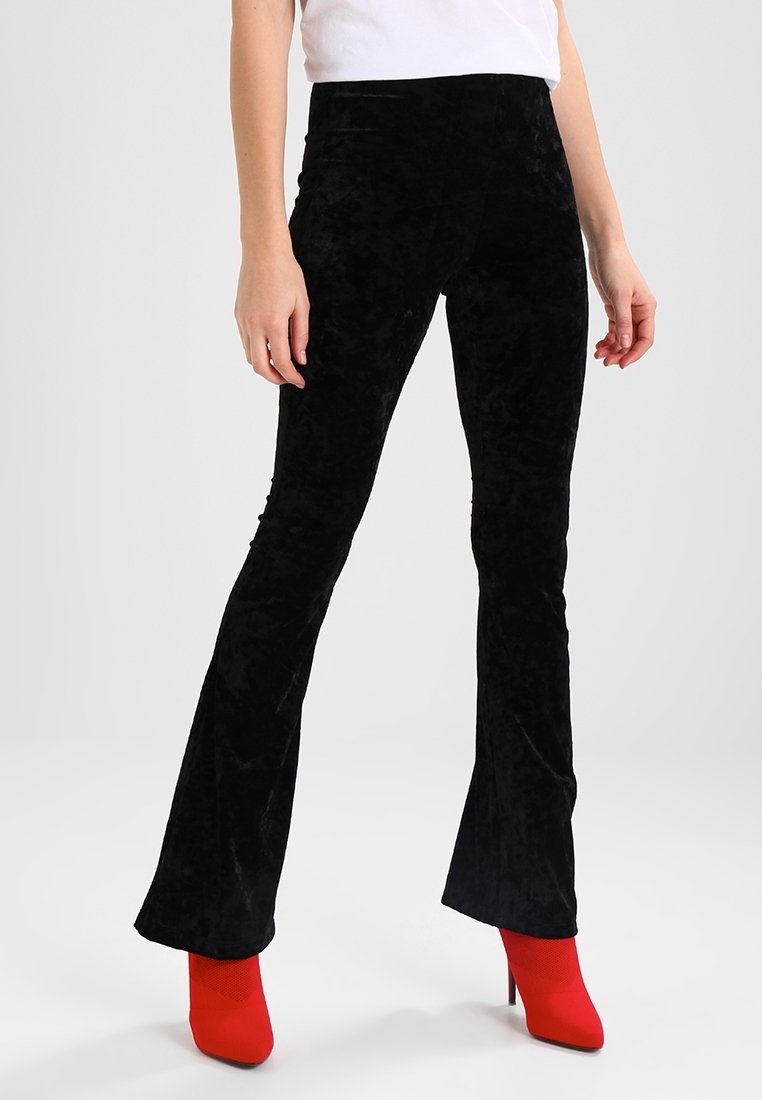 Pantalons en velours noir évasés avec une texture lisse. Dotés d'une taille haute et d'une silhouette ajustée, associés à des talons aiguilles rouges.