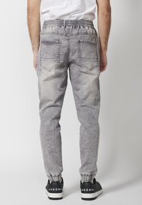 Sive hlače za jogging z zbledelim dizajnom, elastičnim pasom in manšetami na gležnjih. Imajo dve zadnji žepki in subtilno teksturo. Nosi s črnimi supergami.