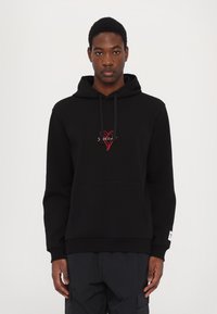 Hoodie noir avec une poche frontale, capuche à cordon de serrage et un logo de cœur rouge brodé sur la poitrine. Présente des poignets et un ourlet côtelés.
