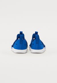 Blaue Sportschuhe mit sleekem Design, aus flexiblem Material gefertigt, mit weißen Sohlen, atmungsaktiven Mesh-Einsätzen und hinteren Zugschlaufen.