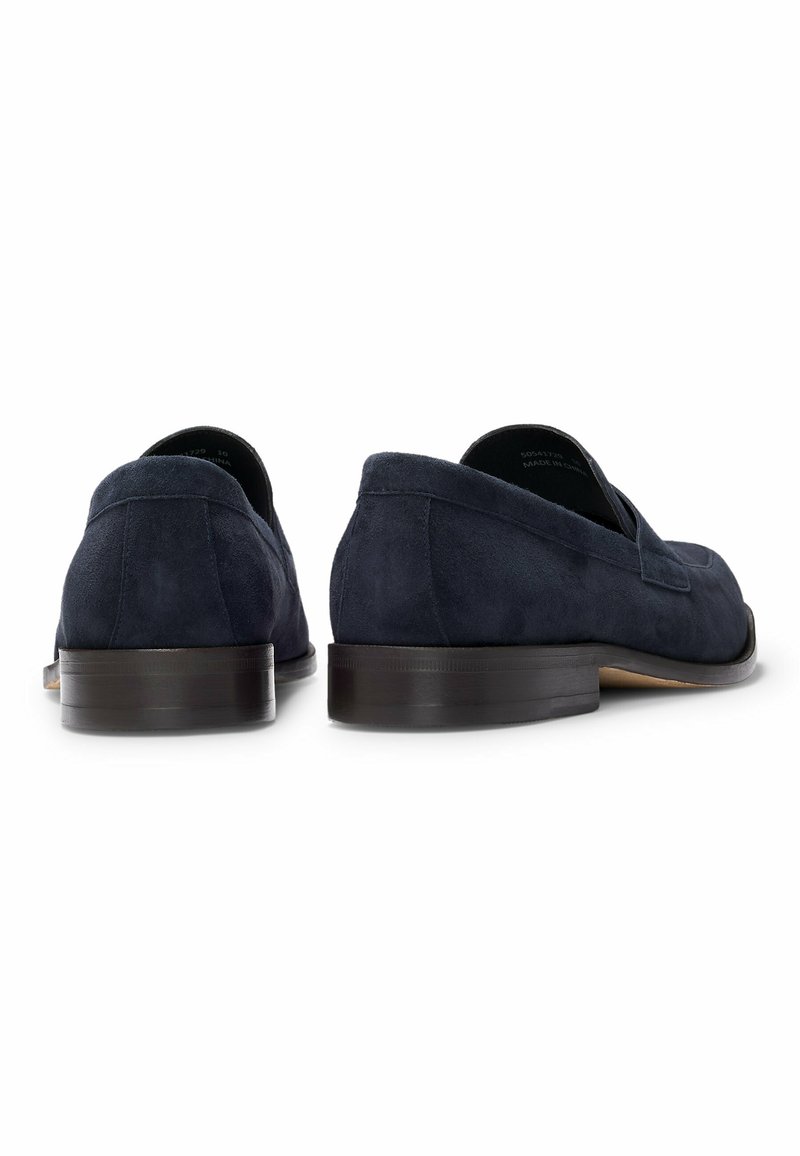 Mocassins en suede bleu marine avec une finition lisse, un petit talon empilé et un minimalisme dans les coutures sur le dessus. La vue arrière met en valeur la forme arrondie.