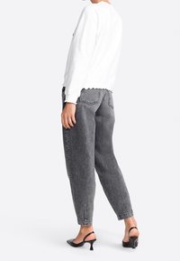 Weißes Sweatshirt mit gewelltem Saum, kombiniert mit hochgerüschten, dunkelgrauen Jeans und schwarzen Slingback-Absätzen. Keine sichtbaren Muster oder Logos.
