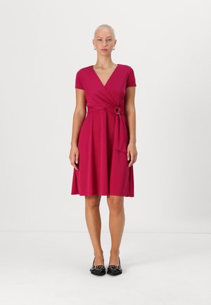 Vestito avvolgente fucsia con maniche corte, presenta un dettaglio annodato in vita e una silhouette a gonna a ruota, abbinato a scarpe nere.