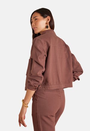 Brown cropped jacket made of cotton blend, featuring a buttoned cuff, shoulder seams, and back yoke detail. Worn over matching pants.