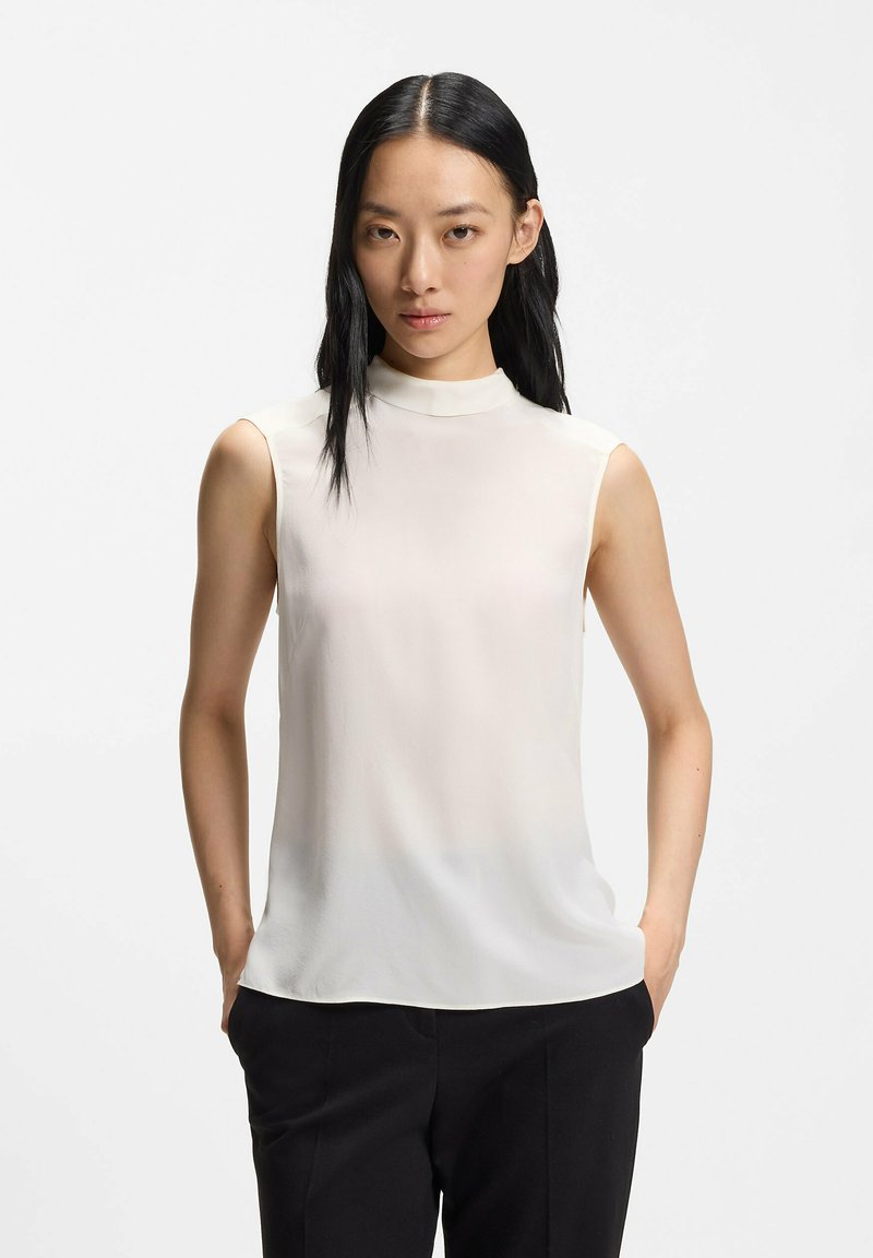 Blusa senza maniche in tessuto bianco morbido con collo alto e silhouette fluida. Tessuto liscio con una leggera lucentezza; senza motivi o accenti.