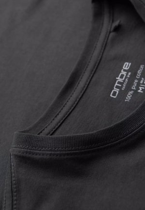 Camiseta de algodón negra con escote redondeado, costuras visibles y una etiqueta que indica 100% algodón puro.