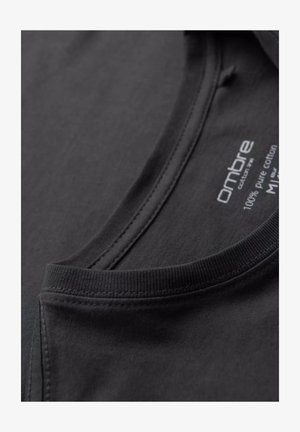 Camiseta de algodón negra con escote redondeado, costuras visibles y una etiqueta que indica 100% algodón puro.