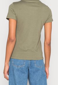 Olivově zelené bavlněné tričko s krátkými rukávy, přiléhavý střih, kulatý výstřih a hladká textura, nošené s světle modrými džínovými kalhotami.
