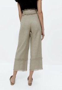 Béžové široké kalhoty s třepeným lemem, vyrobené z texturované látky, s vysokým pasem a poutky na opasek a volným střihem.