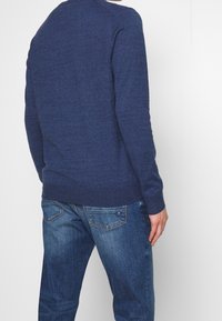 Marineblauwe gebreide trui met een ronde hals en geribbelde manchetten. Gecombineerd met lichte denim jeans, voorzien van achterzakken en subtiele stiksels.