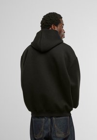 Mustmustest suurusega kapuutsiga dressipluus, millel on reguleeritav kapuuts ja soonikuga mansetid ning alläär. Sile kangas, kantud tumedate teksadega.