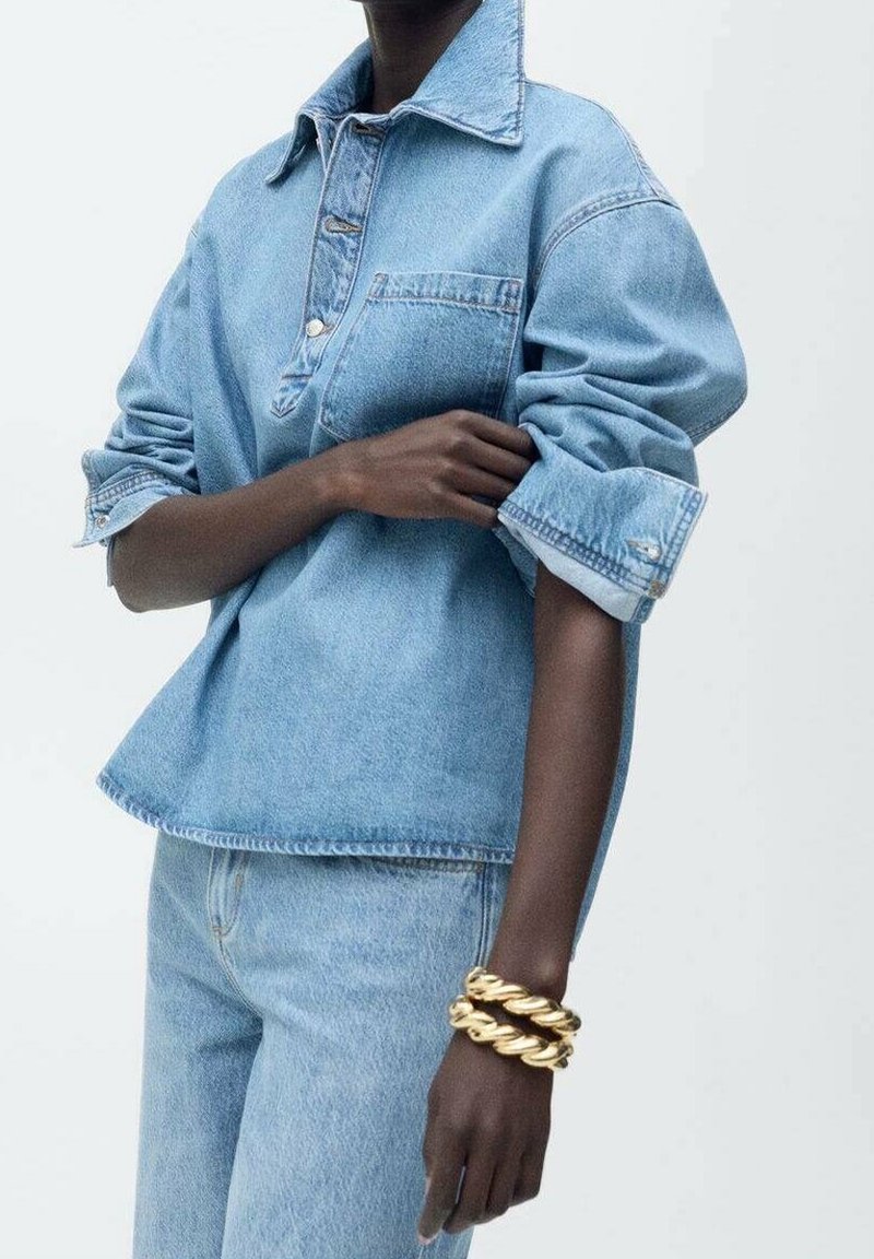 Jasnoniebieska koszula dżinsowa z wyłogowym kołnierzykiem i kieszenią na piersi, z podwiniętymi rękawami. W zestawie z dopasowanymi dżinsami oraz złotymi spiralnymi bransoletkami.