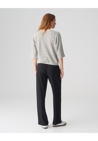 Grauer strukturierter Strickpullover mit drei Viertelärmeln, kombiniert mit schwarzen geraden Hosen und weißen Sneakers. Minimalistisches Design.