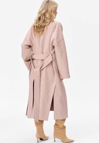 Długi różowy wełniany płaszcz z szerokimi rękawami, paskiem do wiązania i bocznymi rozcięciami; w zestawieniu z beżowymi botkami sięgającymi za kolano oraz miękką fakturą.