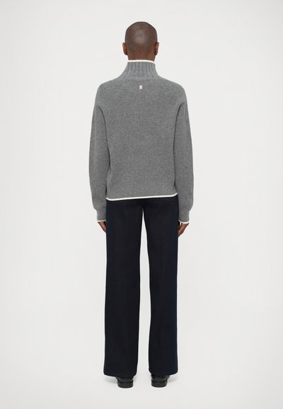 Pull en tricot gris à côtes avec un col haut, doté d'une bordure contrastée blanche à l'ourlet. Porté avec un pantalon large noir.