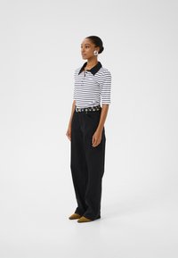 Randig polo-tröja med svart krage, kombinerad med högmidjade svarta jeans och bruna spetsiga skor. Innehåller stora runda silverörhängen.