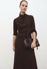 Vestido marrón hasta la rodilla con un cuello alto y mangas largas, acompañado de un bolso marrón oscuro con un cierre dorado y acabado texturizado.