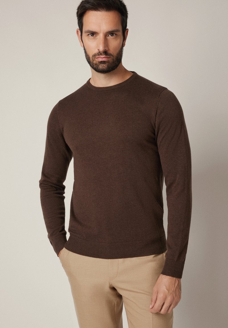 Brązowy sweter z długim rękawem i okrągłym dekoltem, wykonany z miękkiego materiału, o dopasowanym kroju z prążkowanymi wykończeniami na dole.