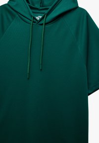 Ciemnozielona bluza z kapturem, wykonana z teksturowanej tkaniny, z regulowanym kapturem, krótkimi rękawami i luźnym krojem.