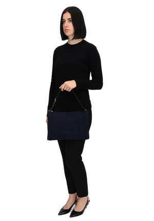 Marineblauwe suede handtas met een rechthoekige vorm, bovenste ritsluiting en een afneembare schouderband, vastgehouden door iemand in het zwart.