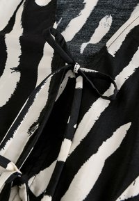 Black and white patterned fabric featuring bold, brushstroke-like stripes with a tie detail at the neckline. Smooth texture, casual design.