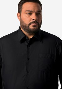 Camicia nera in tessuto liscio, con colletto a punta, chiusura con bottoni, taschino sul petto e maniche lunghe.