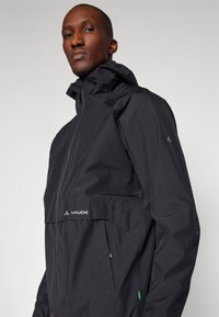 Schwarze wasserdichte Jacke mit hohem Kragen und Reißverschluss. Verfügt über eine Fronttasche und ein Logo auf der Brust. Glatte Textur und athletic Fit.