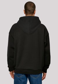Schwarzer Hoodie mit lockerer Passform, großem Kapuzen und weichem Material. Mit ausgefallenen Schultern und geripptem Saum, kombiniert mit blauen Jeans.