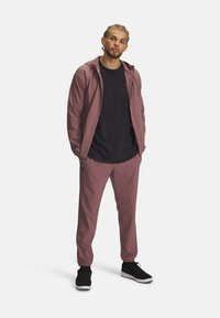 Sportstøj i mauve, lavet af letvægtsmateriale. Har en lynlåshætte, elastiske manchetter og sorte accenter, parret med sorte sneakers.