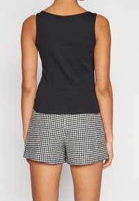 Débardeur noir sans manches associé à un short taille haute avec un motif pied-de-poule noir et blanc. Tissu lisse, coupe décontractée.