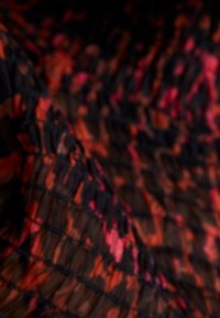 Gros plan d'un tissu texturé avec des motifs abstraits rouges, orange, roses et noirs et une surface plissée et froissée.